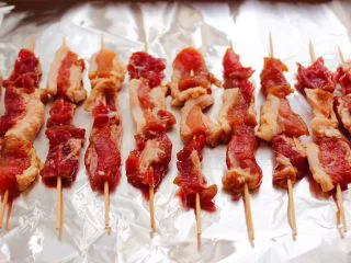 洋葱香烤五花肉,依次串完所有的肉串，把串好的五花肉串平铺在烤盘中，底下铺上锡纸。