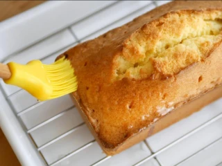 柠檬糖霜磅蛋糕,出炉后的磅蛋糕先放10-15分鐘，时间到脱模，用竹叉在上面戳几个洞，趁蛋糕还热涂上柠檬糖浆，放至完全凉透