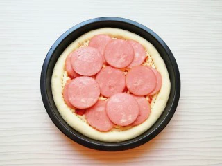 火腿彩蔬披萨,铺上火腿肠片。