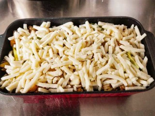 什锦咖喱焗饭,把炒好的米饭铺在容器中。在米饭上面。铺上一层奶酪丝。一定要铺均匀。