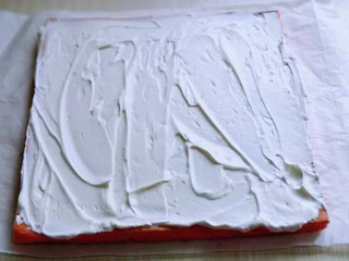 红丝绒草莓奶油蛋糕卷~下午茶必备甜品,将蛋糕片放一张油纸上面,打发的奶油涂抹在蛋糕片上。借助擀面杖和油纸从一段卷起来即可,放入冰箱冷藏1小时以上再切开。(奶油留一些,做装饰用)