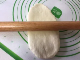 烫种牛奶吐司,取出一个松弛好的面团擀开，擀成牛舌状。
