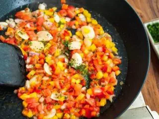 西班牙海鲜饭,平底锅放少许橄榄油，中火将洋葱炒至透明，下蒜瓣和一半欧芹略微翻炒，放入翻切丁及彩椒丁，炒至番茄出汁。