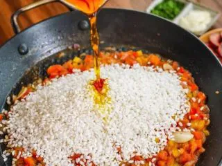 西班牙海鲜饭,放入米，加红椒粉，倒入泡好的藏红花，泡3分钟左右就能显色，翻炒至均匀上色。