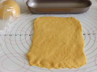 胡萝卜热狗面包,做营养美味早餐,取一个,压平,用擀面杖从中间向俩边擀开。整理成和模具差不多宽度的面片,底部压薄,再卷起来,放入模具中。