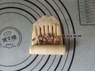 香葱火腿面包卷,在划口的下端地方，放少许香葱火腿碎（要预留些、后面还有用），再自下向上卷起