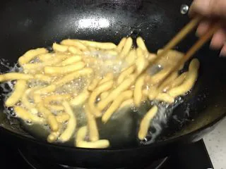 蔓越梅沙琪玛,锅内倒入花生油,煤气灶用小火加热,八分热时放入面条,用筷子翻拌,煎至金黄色捞出。