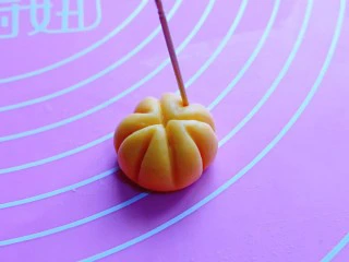 香酥仿真南瓜小饼干,取一小块面团,揉圆,用牙签做出南瓜的形状即可。(首先牙签在面团的中间压出十字,之后再如图中所示,将周边压出南瓜的花纹即可)