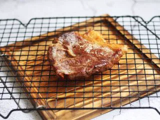 红酒黑胡椒牛排,出锅后放在悬空的蓖网上静置5分钟后再食用。 悬空的蓖网下放一个托盘接渗下来的油和汁水,也避免汁水洗掉表面的焦层。 静置5分钟也可使板腱牛排纤维松弛,让汁水回到肉的组织内,因而牢牢的锁住肉汁,板腱牛排的口感更细嫩。