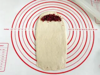 牛奶炼乳蔓越莓软欧,取一份松弛好的面团,用擀面杖擀成长方形,取8克蔓越莓碎放入面片顶端,轻轻压一下。