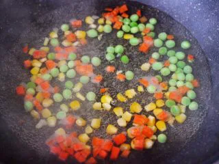 田园时蔬吐司披萨,锅中倒入适量的清水煮沸后，把玉米粒和胡萝卜丁，豌豆倒入锅中进行焯水，煮至1分钟左右捞出沥干水分。