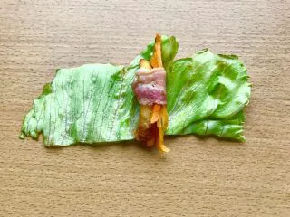 薯条的N种吃法,当培根卷起边就可以出锅了。然后如图先横放着生菜,再上面横放培根,放薯条和叮好的胡萝卜丝,卷起培根。