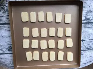 炼乳小饼干(适合新手),冻硬后取出切成厚度均匀的小片并均匀摆入烤盘,不要冻得太硬以免切碎,我用的是不粘烤盘,其它烤盘最好垫一层烘焙纸