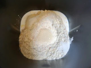 麦片芝麻小餐包,接下来加入高筋面粉和水果麦片,糖和盐对角放,面粉中间挖个小洞放入干酵母,用面粉盖上,选择面包机的“自动和面”程序15分钟。