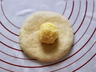 椰蓉奶香面包圈,取一个面团擀成圆形，中间放上称好的椰蓉馅。