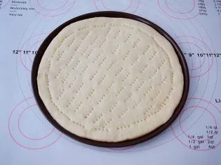 杂蔬火腿肠披萨,把面团取出按压排气,擀成跟披萨盘一样大小的圆形,放入披萨盘,用叉子在饼皮上叉些小洞