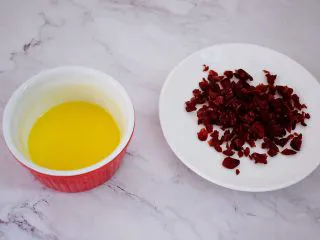 日式炼乳手撕面包,把装饰材料中的黄油和炼乳放入碗中,隔水加热搅拌均匀,这样就做好炼乳酱了,蔓越莓切碎备用