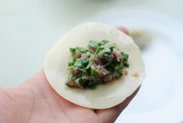 鲜肉韭菜锅贴,取一张水饺皮,铺上韭菜肉馅。