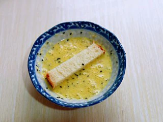 简单快手小零食～黑芝麻椰香吐司条,取一条吐司条，放入蛋液中，均匀裹上蛋液。
