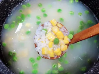 冬日暖心菜 扇贝田园砂锅粥,粥煮至7成熟时，加入豌豆和玉米粒，搅拌均匀，继续小火熬煮。